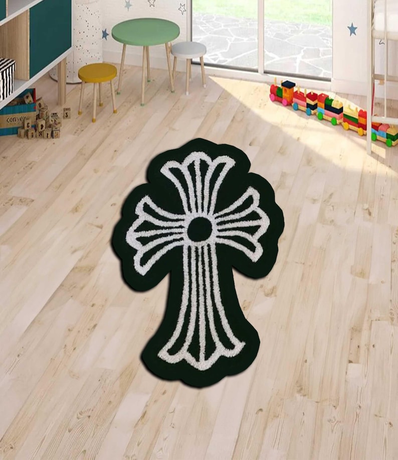 May include: A dark green rug with a white cross design. The rug is placed on a light wood floor. The cross design has a circular center and stylized arms. The rug is a decorative floor covering.