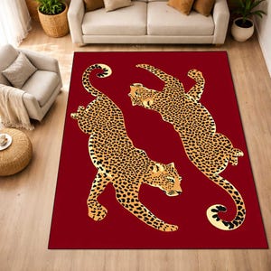May include: A rectangular red area rug featuring two stylized leopard illustrations in shades of gold and black. The leopards are depicted in a dynamic pose, with their bodies arched and tails curled. The rug is designed for home decor.