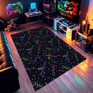 May include: Black rectangular area rug with a colorful confetti and streamer pattern. The rug features neon green, yellow, pink, and blue shapes and lines. The rug is placed on a wooden floor in a gaming room setting.
