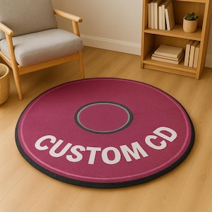 May include: A round rug designed to resemble a CD. The rug is a deep pink color with a black border and a gray inner circle. The words "CUSTOM CD" are printed in white across the rug.