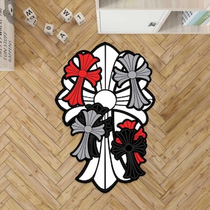 May include: A decorative rug with a white background and a black, red, and gray cross design. The rug has a unique shape and is placed on a wooden floor. The design features multiple crosses with a circular center.