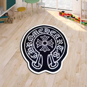 May include: Black and white area rug with a distinctive emblem design. The rug features a central cross-like motif surrounded by stylized text. The rug is placed on a light-colored wooden floor.