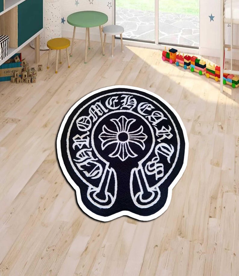 May include: Black and white area rug with a distinctive emblem design. The rug features a central cross-like motif surrounded by stylized text. The rug is placed on a light-colored wooden floor.