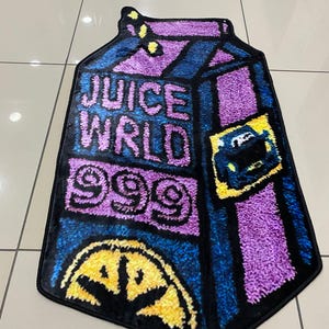 May include: A rectangular rug in the shape of a juice box, featuring the words "JUICE WRLD 999" in white and purple. The rug has a black border and a yellow and black design at the bottom.