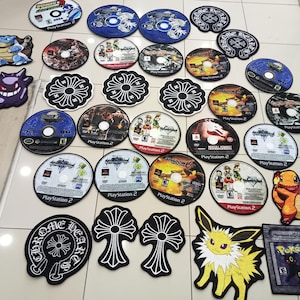 May include: A collection of various round and shaped rugs. The rugs feature designs of video game discs, cartoon characters, and a floral pattern. The colors include blue, black, white, orange, and yellow. The rugs are made of a soft material.