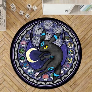 Op de afbeelding: Een rond vloerkleed met een ontwerp in glas-in-loodstijl, voorzien van een centraal zwart Umbreon-personage, een gele maansikkel en een omlijstende rand met diverse cirkelvormige iconen van Eevee-evoluties en kleurrijke bolvormige containers.