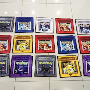 Könnte beinhalten: Eine Sammlung farbenfroher, rechteckiger Teppiche, die wie Vintage Nintendo Game Boy Pokémon-Cartridges aussehen. Jeder Teppich zeigt einen anderen Pokémon-Charakter und das "Pokémon"-Logo, mit "Nintendo Game Boy".