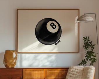 May include: A black and white illustration of a billiard ball with the number 8 on it. The ball is on a white background with the word "Lucky" written below it. The illustration is framed and hanging on a white wall in a living room.