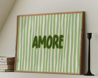 May include: A framed artwork with the word "AMORE" in green, set against a green and white striped background. Two black candle holders stand to the right of the artwork. A stack of books is on the left.