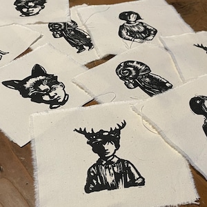 Può includere: Un set di 10 toppe di tessuto stampate in bianco e nero con varie illustrazioni di persone e animali. Le toppe sono su uno sfondo bianco e hanno una superficie ruvida e testurizzata.
