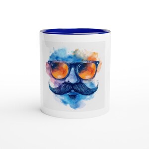 May include: White ceramic mug with a blue rim. The mug features a watercolor illustration of a face with a mustache and sunglasses. The sunglasses have orange lenses.