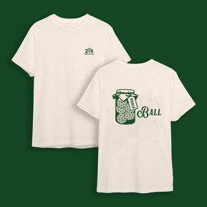 May include: Off-white t-shirts with green graphics. One shirt has a small logo on the front, the other features a jar of pickles with a tag that says "Pickle" and the word "Ball".