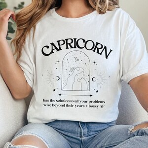Puede incluir: Camiseta blanca con un gr&aacute;fico negro de un signo zodiacal de Capricornio y el texto "CAPRICORN has the solution to all your problems wise beyond their years - bossy AF".