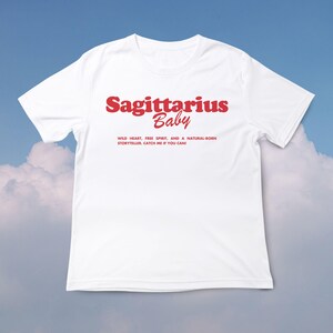 May include: White t-shirt with red text that says "Sagittarius Baby" and "Wild heart, free spirit, and a natural-born storyteller, catch me if you can!"