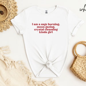 K&ouml;nnte beinhalten: Wei&szlig;es T-Shirt mit dem Text "I am a sage burning, moon gazing, crystal cleansing kinda girl" in Rot.