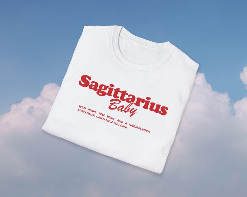 May include: White t-shirt with red text that reads "Sagittarius Baby" and a description below: "WILD HEART, FREE SPIRIT, AND A NATURAL-BORN STORYTELLER. CATCH ME IF YOU CAN!"