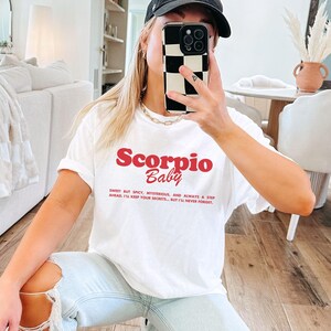 May include: White t-shirt with red text that reads "Scorpio Baby" and a quote about Scorpio traits.