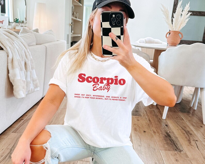 May include: White t-shirt with red text that reads "Scorpio Baby" and a quote about Scorpio traits.
