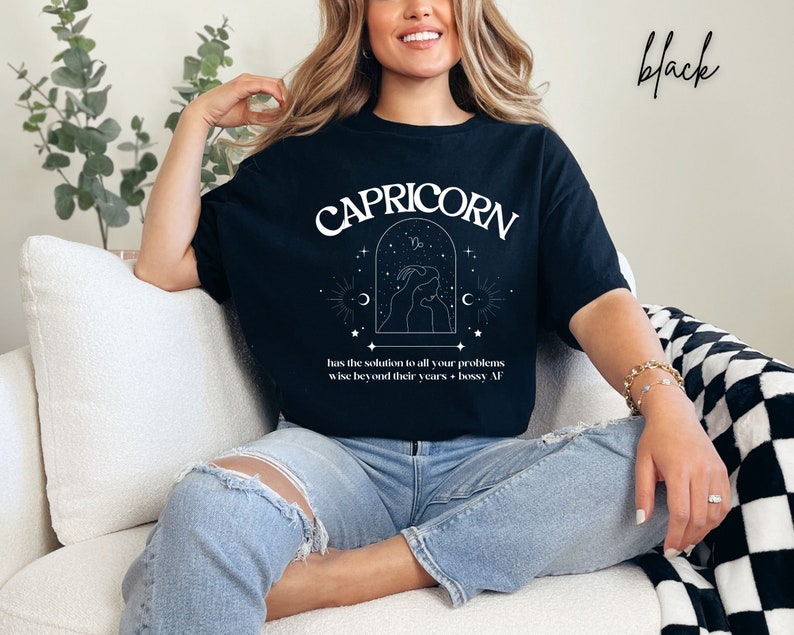 Puede incluir: Camiseta negra con un dise&ntilde;o gr&aacute;fico blanco que representa el signo del zod&iacute;aco Capricornio. El gr&aacute;fico incluye el texto "CAPRICORN" y la frase "has the solution to all your problems wise beyond their years - bossy AF".