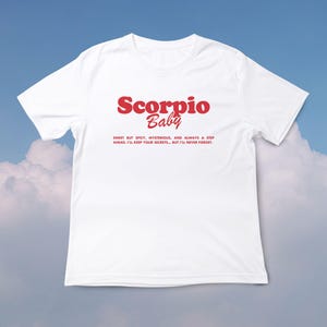 May include: White t-shirt with red text that reads "Scorpio Baby" and a short description about the zodiac sign.