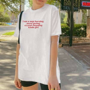 K&ouml;nnte beinhalten: Wei&szlig;es T-Shirt mit dem Text "I am a sage burning, moon gazing, crystal cleansing kinda girl" in Rot gedruckt.
