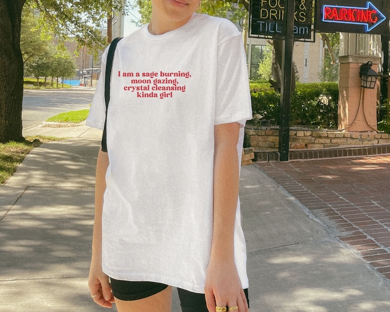 K&ouml;nnte beinhalten: Wei&szlig;es T-Shirt mit dem Text "I am a sage burning, moon gazing, crystal cleansing kinda girl" in Rot gedruckt.