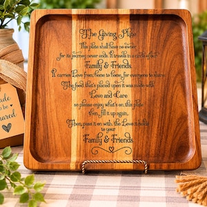 May include: A square wooden serving tray with rounded corners, featuring engraved text about sharing food with family and friends. The tray is supported by a metal stand and has a light and dark wood grain pattern. A gift tag reads "Made to be Shared."