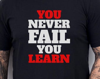 May include: Black crew neck t-shirt with the text "YOU NEVER FAIL YOU LEARN" in white and red block letters. The shirt is worn by a person with tattoos on their arm.