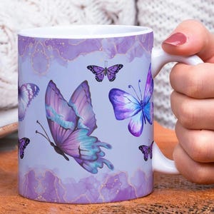 May include: A white ceramic mug with a purple and blue butterfly design. The mug has a watercolor-like background with gold accents.
