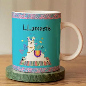Op de afbeelding: Een turquoise blauwe keramische mok met een roze rand en een witte lama-illustratie. De lama draagt ​​een bloemenkrans en staat in een yogahouding. De tekst "Llamaste" is in zwart op de mok gedrukt.