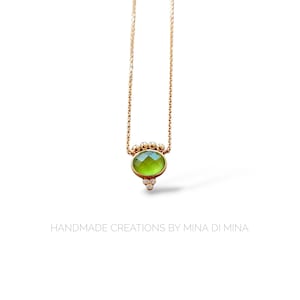 Puede incluir: Un delicado collar de cadena de oro con un colgante de piedra preciosa verde rodeado de pequeños diamantes. El colgante tiene forma ovalada y un diseño facetado.