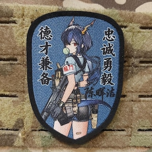 Peut inclure: Un écusson bleu et noir représentant un personnage de style anime tenant une arme à feu, mâchant du chewing-gum et du texte en caractères chinois. L'écusson a une bordure noire et est rectangulaire, sur fond camouflage.