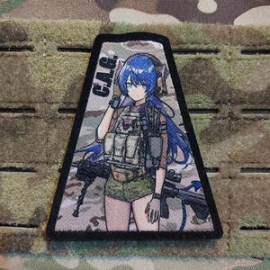 Może przedstawiać: Czarna naszywka z postacią anime z niebieskimi włosami, ubraną w wojskowy strój i trzymającą broń. Na naszywce widnieje napis "C.A.G." na tle kamuflażu.