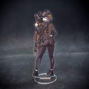 May include: A clear acrylic standee of an anime-style female character in tactical gear, holding a rifle. The character is viewed from behind, wearing a helmet, vest, and black leggings. The standee has a clear circular base.