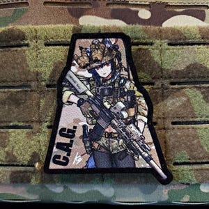 Puede incluir: Un parche con una ilustración de estilo anime de un soldado con uniforme de camuflaje, sosteniendo un rifle. El parche tiene las letras "C.A.G." impresas. El fondo es un patrón de camuflaje.