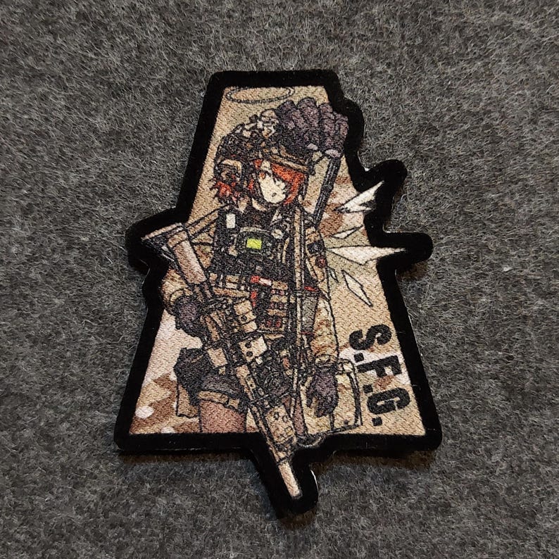 May include: A triangular patch featuring a cartoon image of a female soldier holding a rifle. The soldier is wearing a helmet, tactical gear, and a camouflage uniform. The patch has a brown and tan camouflage pattern and the text "S.F.G." in black.
