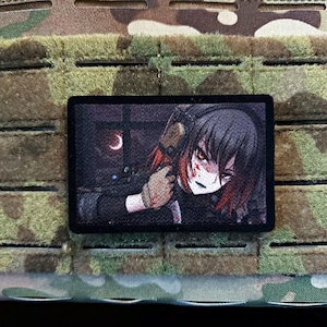 Könnte beinhalten: Ein rechteckiger Aufnäher mit einer Anime-Illustration eines Charakters mit schwarzen Haaren, roten Highlights und Blut im Gesicht, der eine Waffe hält. Der Aufnäher ist vor einem Tarnhintergrund angebracht.