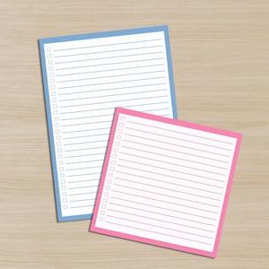 May include: Two notepads, one blue and one pink, rest on a light wood-grain surface. The blue notepad is larger and rectangular, with a blue border, horizontal lines, and check boxes. The pink notepad is smaller and square, with a pink border.