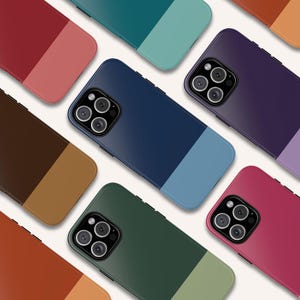 Op de afbeelding: Een verzameling kleurrijke telefoonhoesjes in verschillende tinten, waaronder rood, bruin, groen en blauw. Elke hoes heeft een tweekleurig ontwerp met een contrasterend kleurblok aan de onderkant. De hoesjes hebben meerdere cameralenzen.