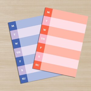 May include: Two rectangular weekly planner notepads. One is blue and lavender, the other is coral and pink. Each notepad has columns for the days of the week, labeled M, T, W, TH, F, S, and SU. The notepads are on a light wood grain surface.