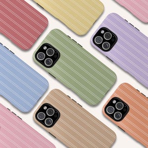 Può includere: Una collezione di custodie per telefoni colorate con un motivo a righe bianche. Le custodie, in varie tonalità pastello come rosa, blu, verde e giallo, presentano un modulo fotocamera con più lenti.