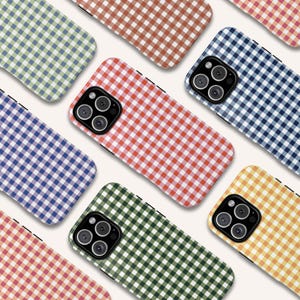 Puede incluir: Una colección de fundas para teléfonos con un patrón de cuadros vichy en varios colores, incluyendo rojo, azul, verde, amarillo y marrón. Las fundas tienen un diseño elegante y un recorte para la cámara.