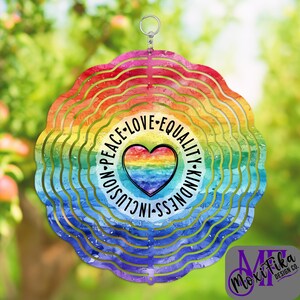 May include: A rainbow-colored wind spinner with a heart-shaped graphic. The graphic includes the words "Peace, Love, Equality, Kindness, Inclusion." The wind spinner has a scalloped edge and a silver hanging loop.