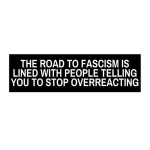 May include: A rectangular black sticker featuring white, capitalized, sans-serif text that reads: THE ROAD TO FASCISM IS LINED WITH PEOPLE TELLING YOU TO STOP OVERREACTING. The design is simple, bold, and high-contrast, presenting a clear political message.
