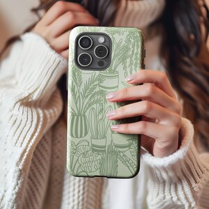 May include: A white phone case with a green and white design of potted plants. The case has a camera lens cutout and a black border.