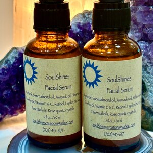 Puede incluir: Dos botellas de vidrio &aacute;mbar con goteros negros, etiquetadas como "SoulShines Facial Serum". Las botellas est&aacute;n sobre una rodaja de &aacute;gata gris claro y marr&oacute;n. Las etiquetas enumeran los ingredientes, que incluyen aceite de jojoba, aceite de almendras dulces, aceite de aguacate, hibisco, aceite de rosa mosqueta, vitamina E y C, retinol, &aacute;cido hialur&oacute;nico, aceites esenciales y cristales de cuarzo rosa. Las botellas son de 2 fl oz / 60 ml e incluyen la informaci&oacute;n de contacto SoulShinescreations@yahoo.com y (702) 415-6171.