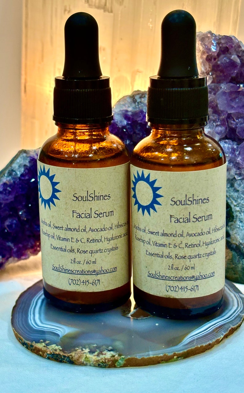 Puede incluir: Dos botellas de vidrio &aacute;mbar con goteros negros, etiquetadas como "SoulShines Facial Serum". Las botellas est&aacute;n sobre una rodaja de &aacute;gata gris claro y marr&oacute;n. Las etiquetas enumeran los ingredientes, que incluyen aceite de jojoba, aceite de almendras dulces, aceite de aguacate, hibisco, aceite de rosa mosqueta, vitamina E y C, retinol, &aacute;cido hialur&oacute;nico, aceites esenciales y cristales de cuarzo rosa. Las botellas son de 2 fl oz / 60 ml e incluyen la informaci&oacute;n de contacto SoulShinescreations@yahoo.com y (702) 415-6171.