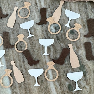 May include: Assortment of brown, beige, and white confetti cutouts. The cutouts include cowboy boots, champagne flutes, and rings with diamonds.