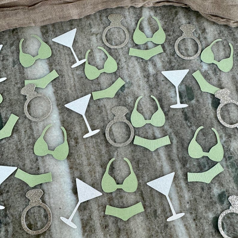 May include: Green and silver confetti featuring images of a bikini, a martini glass, and a ring. The confetti is perfect for a bachelorette party.