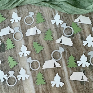 May include: White and green confetti with camping and engagement ring designs. The confetti includes images of tents, trees, campfires, and engagement rings.